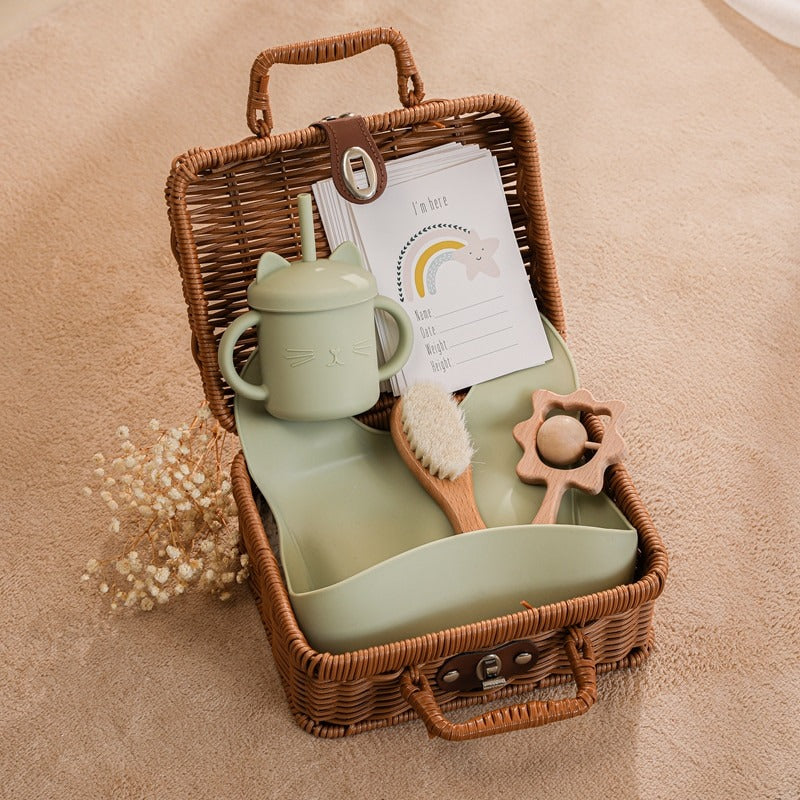 Green bundle of silicone toys and feeding accessories for the new baby in a rattan suitcase