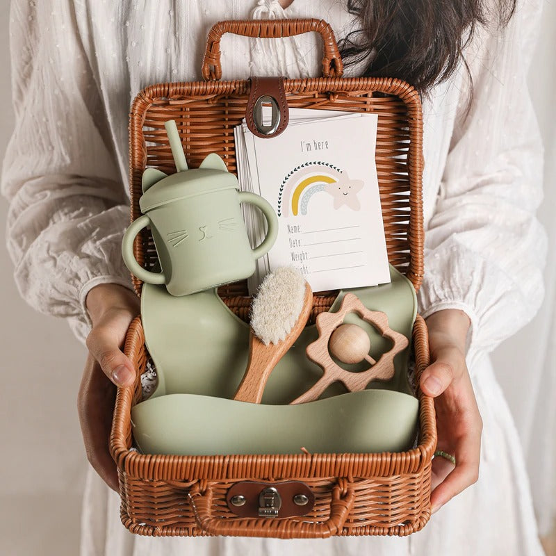 Green bundle of silicone toys and feeding accessories for the new baby in a rattan suitcase